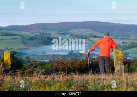 Morning hill walker taking in the beautiful landscape scenery overlooking rural upland farming land of Flintshire towards the misty landscape of the Clwydian Range hills on the Flintshire Side of the Range, Wales, UK Stock Photo