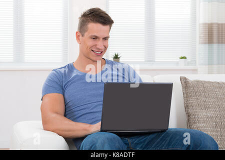 Young Man Using Laptop While Sitting On Sofa Stock Photo
