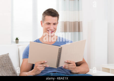 Portrait Of Young Happy Man With Photo Album Sitting On Sofa Stock Photo