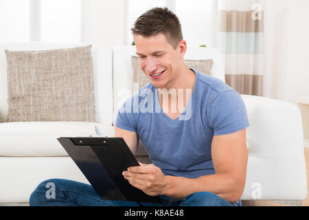Young Man Writing On Clipboard At Home Stock Photo