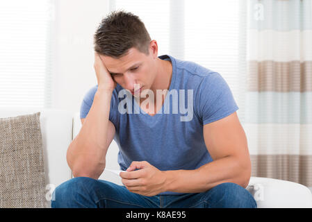 Young Man On Sofa Checking His Body Temperature With Thermometer Stock Photo