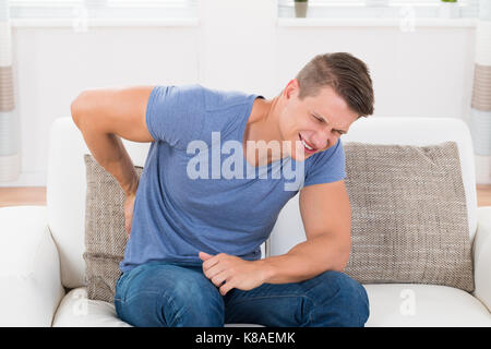 Young Man On Sofa Suffering From Backpain At Home Stock Photo