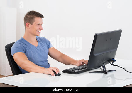 Young Man Working On Desktop Computer At Desk Stock Photo