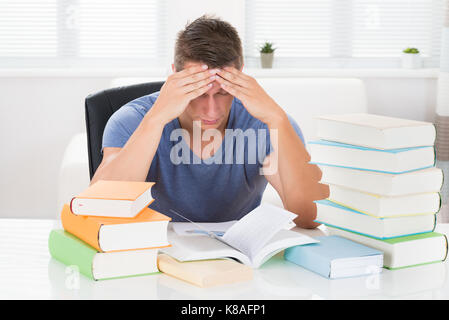 Portrait Of Tired Young Man Studying Books At Desk Stock Photo