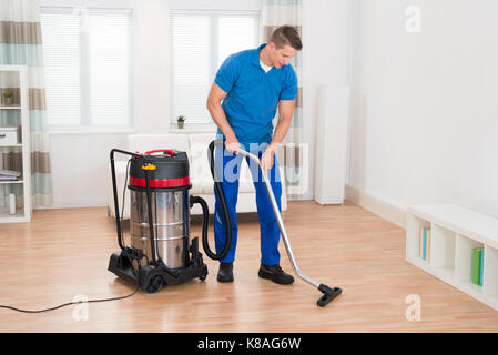 Happy Male Janitor Vacuuming Wooden Floor In House Stock Photo