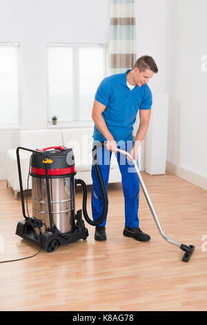 Happy Male Janitor Vacuuming Wooden Floor In House Stock Photo