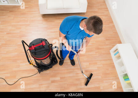 High Angle View Of Male Janitor Cleaning Floor With Vacuum Cleaner Stock Photo