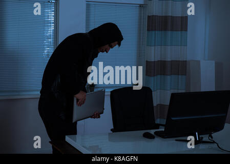 Male Thief Stealing Laptop From Office At Night Stock Photo