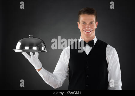 Portrait Of Happy Waiter Holding Stainless Steel Cloche Over Tray Stock Photo