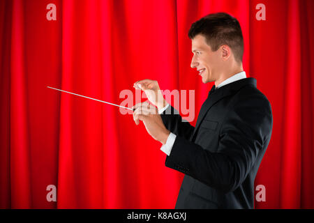 Male Orchestra Conductor Holding Baton Over Red Curtain Stock Photo