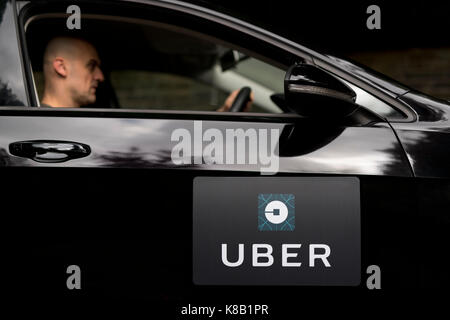A black Volkswagen featuring the Uber logo is used as a taxi and also shows a driver in a leafy suburban street in the UK (Editorial use only). Stock Photo