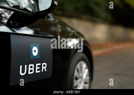 A black Volkswagen featuring the Uber logo is used as a taxi and also shows a driver in a leafy suburban street in the UK (Editorial use only). Stock Photo