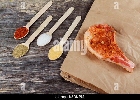 Raw pork steaks on wooden board with herbs, garlic, spices and tomatoes ready for cooking. Selective focus. Stock Photo