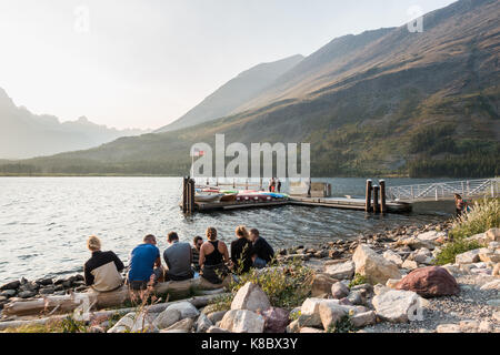 Tourists / visitors enjoying the late afternoon outside the Swiftcurrent Lodge and the edge / shore of the Swiftcurrent Lake in Glacier National Park Stock Photo