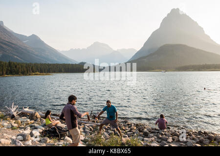 young men enjoying the late afternoon the edge / shore of the Swiftcurrent Lake in Glacier National Park Stock Photo