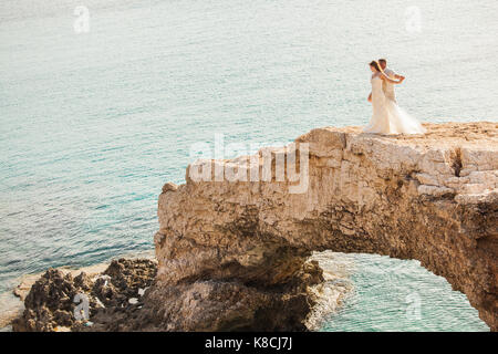 beautiful gorgeous blonde bride and stylish groom standing on rocks, on the background of a sea, wedding ceremony on cyprus. Stock Photo
