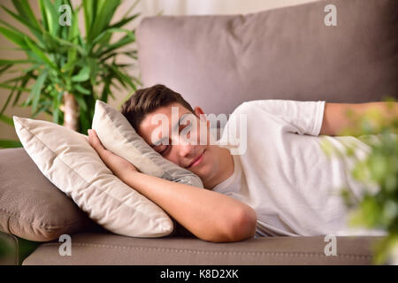 Man napping happily lying on a couch with cushions at home. Front view Stock Photo