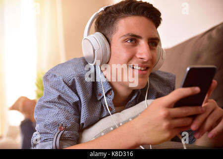 Teen listening music with headphones from mobile lying face down on couch Stock Photo