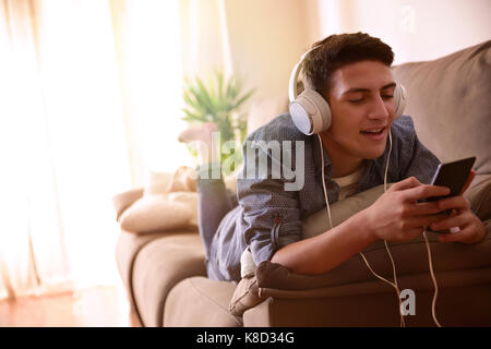 Teen listening and singing music with headphones from mobile lying face down on couch Stock Photo