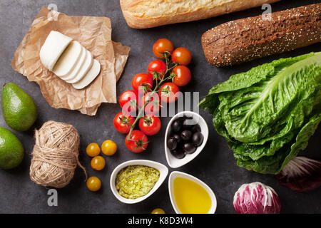 Ciabatta sandwich cooking with romaine salad, prosciutto and mozzarella cheese over stone background. Top view Stock Photo