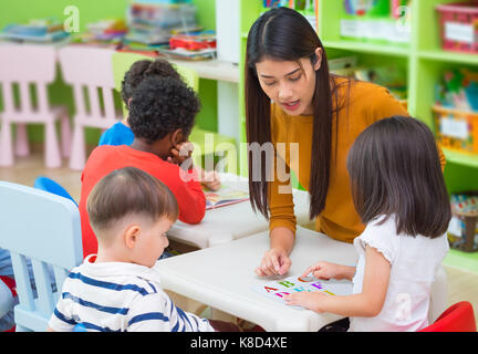 Asian female teacher teaching mixed race kids reading book in classroom,Kindergarten pre school concept. Stock Photo