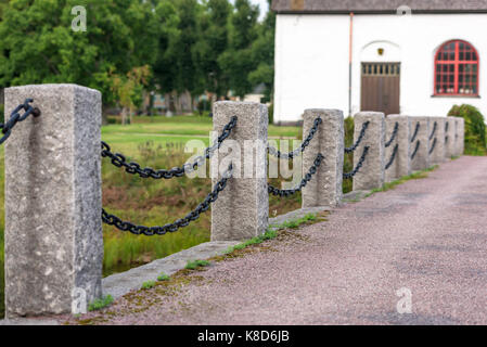 Stone pillars and iron chain as railing along road. Church in background. Stock Photo