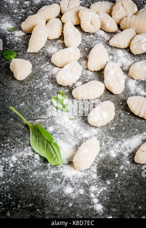 Raw uncooked homemade potato gnocchi with flour, grated parmesan cheese, basil and pesto sauce. On concrete grey background, copy space Stock Photo