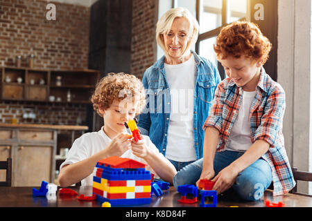 Careful elderly lady watching grandchildren playing at home Stock Photo