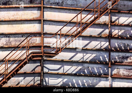 Concrete cylindrical industrial silo with metal stairs with safety railing and large bore pipes. Stock Photo