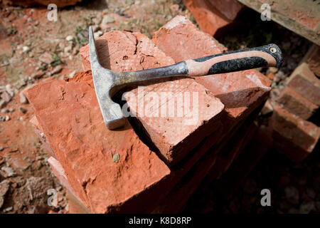 Pile of red clay handmade bricks with brick splitting hammer. Stock Photo