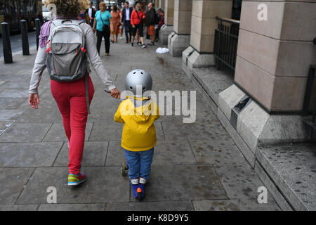 Brightly clothed Mother and son walks hand in hand  in London England carrying aand riding a scooter Stock Photo