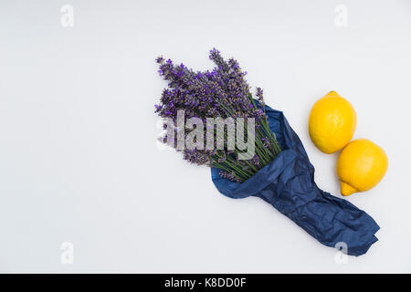 Bouquet of purple fresh fragrant lavender wrapped in blue paper with two fresh yellow lemons on white background Stock Photo