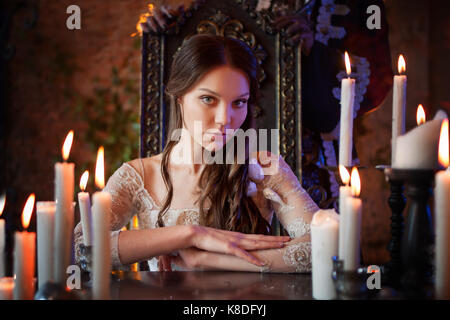 Beautiful young woman in vintage dress, at a table in the mystic manor Stock Photo