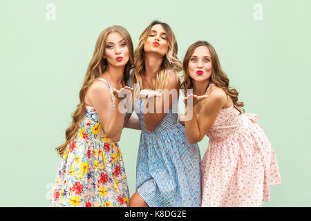 Sending air kiss. Three best friends posing in studio, wearing summer style dress against green background. Girls smiling and having fun. Studio shot  Stock Photo