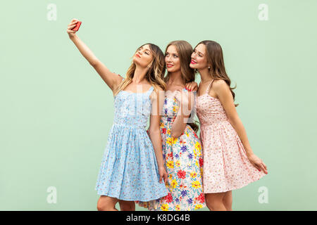 Hipsters three friends in casual dress, macking selfie on green background and have fun. Studio shot Stock Photo