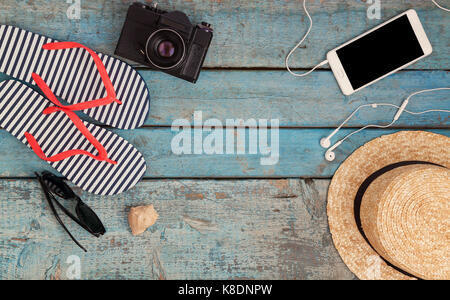 Still life of different items for relaxing on the beach, rubber flip-flops, hat, camera, phone, sunglasses, headset on a wooden blue background. Conce Stock Photo
