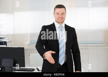 Portrait of happy businessman offering handshake while standing at computer desk in office Stock Photo