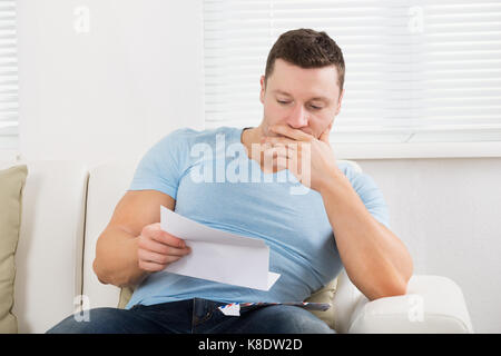 Serious mid adult man reading letter on sofa at home Stock Photo
