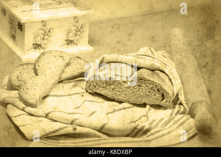 Bread loaf wrapped in a kitchen towel, rolling pin, and two slices of bread lying on the cloth. Decoupage box is partially visible. Selective focus. Stock Photo