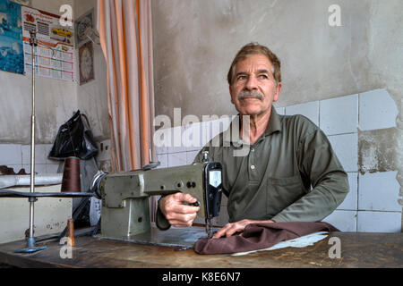 Fars Province, Shiraz, Iran - 18 april, 2017: An elderly tailor man in a tailor's shop sews, using a sewing machine. Stock Photo