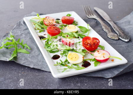 Fresh radish, cherry tomato, quail egg, rucola with balsamic glaze on a white plate. Mediterranean lifestyle. Healthy food. Stock Photo