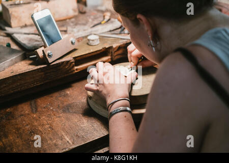 Over shoulder view of female jeweller engraving metal at workbench Stock Photo