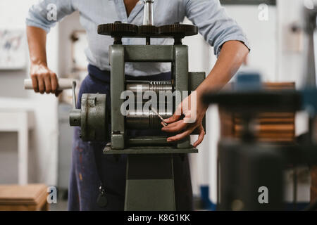 Mid section of female jeweller winding metal rod through machine in jewellery workshop Stock Photo