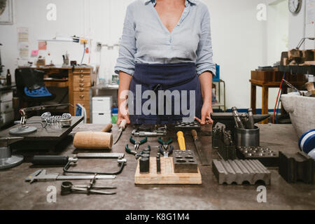 Mid section of female jeweller laying out hand tools at workbench in jewellery workshop Stock Photo