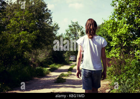 Rear view of teenage girl strolling along rural dirt track Stock Photo