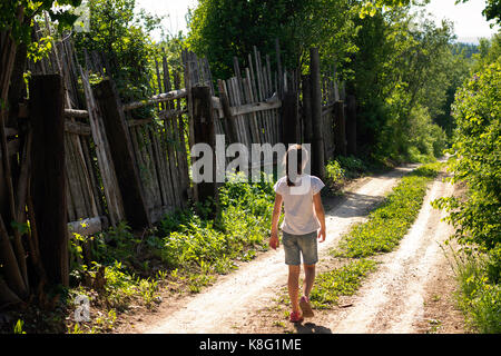 Rear view of lone teenage girl strolling along rural dirt track Stock Photo