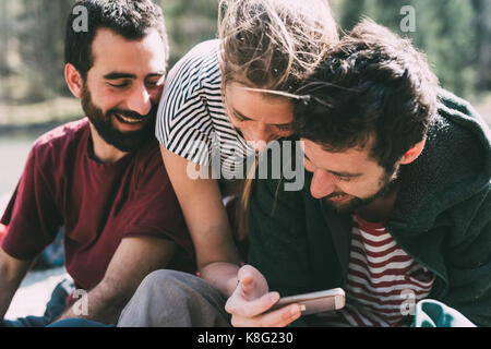 Three young adult friends looking and laughing at smartphone, Lombardy, Italy Stock Photo