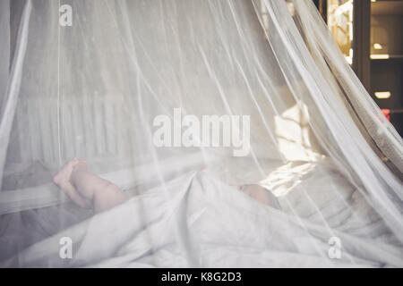 Baby girl lying in net draped crib grasping bed sheet Stock Photo