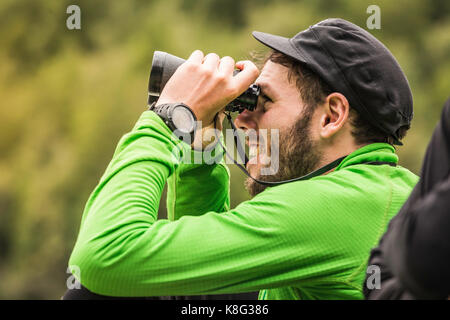 Young male backpacker looking through binoculars in Queulat National Park, Chile Stock Photo