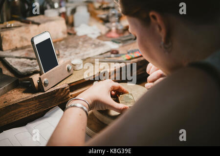 Over shoulder view of female jeweller engraving metal at workbench Stock Photo